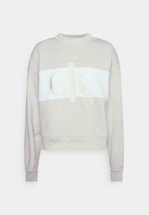 Licht beige cropped sweatshirt met witte horizontale streep en groot geborduurd "CK"-logo aan de voorkant, lange mouwen en geribbelde boorden.