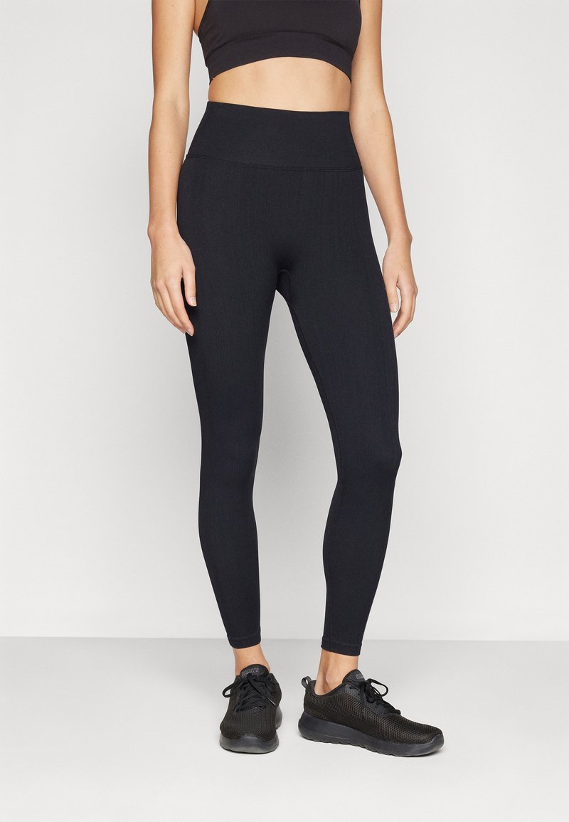 Svarta träningsleggings med hög midja, ribbad textur och en åtsmitande design. Bärs med svarta sneakers.