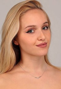 Silberkette mit einem eleganten, geschwungenen Design, die auf nackter Haut getragen wird; Person mit langen, glatten blonden Haaren und natürlichem Make-up.