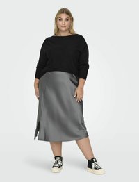 Melns džemperis ar plašu kakla izgriezumu un garām piedurknēm, apvienots ar pelēku zīda svārku līdz ceļgaliem ar sānu spraugu, valkāts ar melniem sporta apaviem.