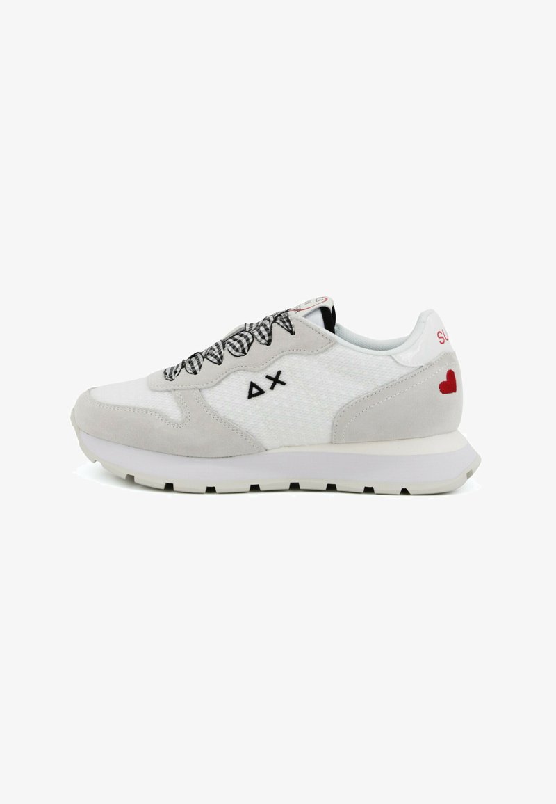 Zapatilla blanca y gris con cordones a cuadros blancos y negros, logo de triángulo y X en negro, y un pequeño corazón rojo en el talón.
