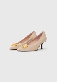 Décolleté beige con punta a mandorla, caratterizzate da una dettagliata catena dorata sulla tomaia e da una texture liscia e elegante. Design con tacco basso.