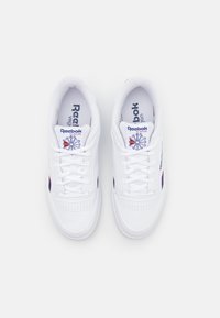 Sapatilhas brancas em couro com uma textura lisa, apresentando uma ponta perfurada, atacadores brancos e a marca Reebok Classic na língua e nos lados.