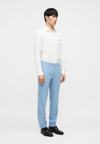 Chemise blanche à manches longues avec boutons sur le devant, pantalon bleu clair taillé sur mesure, et chaussures noires ; tissu lisse avec une coupe ajustée. Design minimaliste.