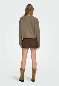 Pull marron court, mini jupe en daim marron et bottes de cow-boy beiges. Texture lisse et coupe décontractée avec un col rond.