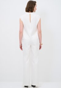 Top bianco senza maniche con dettaglio a forma di chiave sulla schiena, abbinato a pantaloni bianchi a gamba larga. Tessuto dalla consistenza liscia, design minimalista.