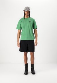 Grøn bomulds t-shirt, løs pasform, parret med sorte denim shorts. Grå kasket med farverig broderi foran, sorte læder ankelstøvler.