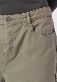 Χακί παντελόνια με λεία υφή, που διαθέτουν κλασικό σχέδιο πέντε τσεπών, κλείσιμο με κουμπί μπροστά και διακριτές λεπτομέρειες ραφής.
