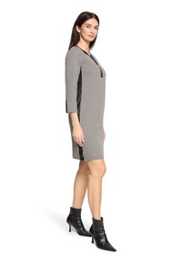 Grijs-zwart jurkje met patroon en driekwart mouwen, voorzien van een zwart zijpaneel en een eenvoudige halslijn. Gecombineerd met zwarte enkellaarsjes.