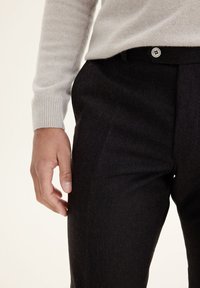 Gray cashmere sweater with long sleeves paired with black wool trousers featuring a button closure and a smooth, textured surface.