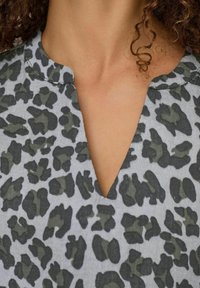 Grå stof med leopardprint i mørkegrøn og sort, med V-udskæring og kort, buet krave.