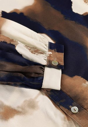Zijden shirt met een bruine, marineblauwe en crèmekleurige abstracte patroon. Lange mouwen met geplooide details en een knoopsluiting bij de manchetten.