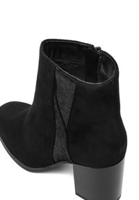 Bota negra de ante hasta el tobillo con paneles laterales elásticos, punta redondeada y tacón bajo de bloque. Cuenta con una cremallera para facilitar su uso.