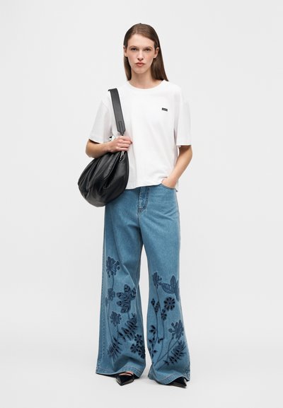 Λευκό βαμβακερό T-shirt με μικρό μαύρο λογότυπο. Μπλε τζιν παντελόνι φαρδιάς γραμμής με ναυτικό κεντητό σχέδιο με λουλούδια. Μαύρη επιμελώς χαλαρή τσάντα και μυτερές γόβες.