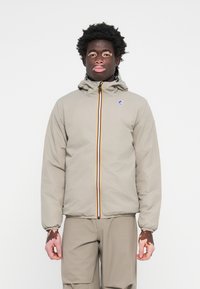 Veste zippée beige clair avec capuche, dotée d'une bande verticale multicolore, de poignets élastiques et d'un logo sur la poitrine gauche.