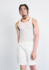 White ribbed tank top with a round neckline paired with white shorts featuring an elastic waistband and logo patch on the leg.