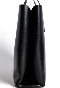 Borsa tote alta in pelle nera con manici sottili e texture liscia, mostrata di profilo contro uno sfondo bianco.
