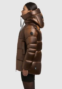 Jachetă puffer din material lucios de culoare maro, dotată cu un guler înalt, buzunare cu fermoar și accente negre cu logo. Design gros, matlasat pentru izolare.