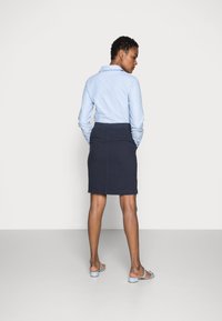 Chemise à manches longues bleu clair avec un col, associée à une jupe crayon bleu marine et des sandales à semelles légères bleu clair, vue de l'arrière.
