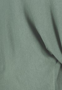 Teal gebreide stof met een zachte textuur, voorzien van subtiele ribbels en hangende plooien, waardoor een gelaagd uitzicht ontstaat.