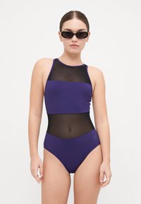 Maillot de bain deux pièces violet avec un col halter, des sections en maille et un bas taille haute. Texture lisse avec des couleurs contrastées.