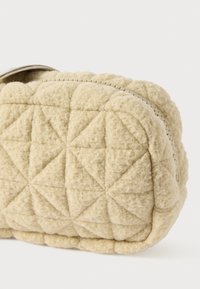 Quilted cremefarvet taske med en rund form, lavet af tekstureret stof. Har trekante mønstre og lynlås lukning.