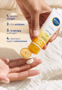 NIVEA SUN Anti-Age Q10 Sonnencreme in einer weißen Tube mit gelber Kappe, die eine weiße Creme auf eine Hand gibt. Anweisungen in blauer Schrift.