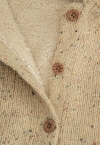 Dzianinowy kardigan w kremowym kolorze z teksturowaną powierzchnią, wyposażony w miękką, polarową podszewkę i brązowe, drewniane guziki.