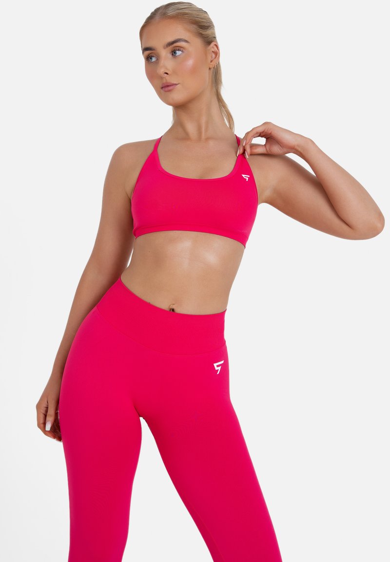 Reggiseno sportivo rosa e leggings a vita alta realizzati in materiale liscio ed elastico. Presenta spalline sottili e un logo bianco sulla vita.