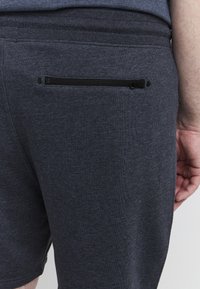 Tamno sive kratke hlače izrađene od mekog pamuka. Imaju zatvoren džep na leđima sa crnim patentnim zatvaračem, glatku teksturu i uski kroj.