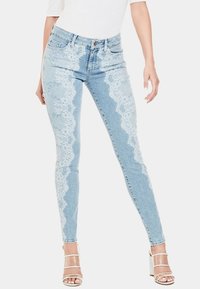 Vaqueros de mezclilla de cintura alta en azul claro con detalles de encaje en los laterales y un ajuste slim. Presenta una cremallera y un cierre de botón en la parte delantera.