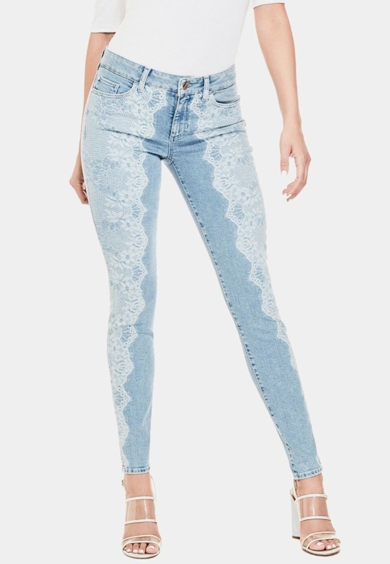 Vaqueros de mezclilla de cintura alta en azul claro con detalles de encaje en los laterales y un ajuste slim. Presenta una cremallera y un cierre de botón en la parte delantera.