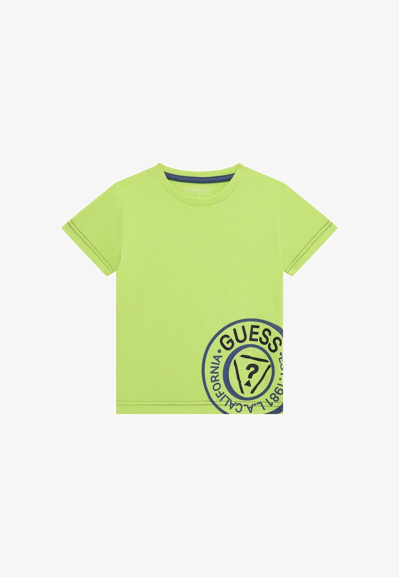 T-shirt di cotone verde lime con maniche corte, colletto rotondo e grafica circolare blu del logo "GUESS" sul davanti, che presenta l'anno 1981.
