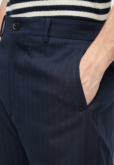 Pantaloni blu navy a righe sottili con una superficie liscia, tasche laterali e chiusura con bottone. Il materiale sembra leggero e su misura.