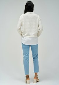 Pull en maille texturée blanc, superposé à une chemise blanche. Jean droit bleu clair, sandales à talons carrés taupe. Vue de dos.