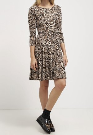 Luipaardprintjurk met driekwart mouwen, aansluitende taille en uitlopende rok. Draagt met zwarte schoenen en sokken voor contrast.