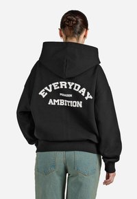 Felpa nera con cappuccio che presenta un testo bianco sul retro che dice "EVERYDAY AMBITION" con "PEGADOR" sottostante. Vestibilità casual, polsini e fondo a costine.