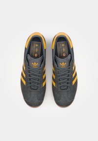 Black and gray suede sneakers with yellow stripes, featuring a rounded toe, cushioned tongue, and textured rubber sole.