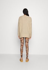 Beżowy sweter dzianinowy o luźnym kroju, z długimi rękawami. Getry w odcieniach brązu, z kwiatowymi wzorami i tekstem. Widać lekkie obuwie.