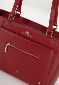Rode leren handtas met een korrelige textuur, gouden hardware-accenten en een ritsvak aan de voorkant. Voorzien van dubbele handgrepen bovenaan en een logo-detail.