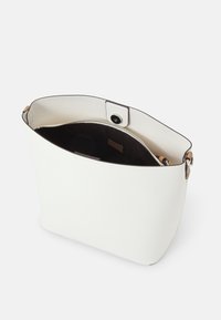 Vit fusk läder bucket bag med en mörk inredning, en magnetisk snap-stängning och ljusbruna accenter på remmarna och inredningsetiketten.