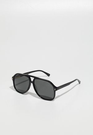 Schwarze Sonnenbrille mit einem achteckigen Rahmen, dunklen Gläsern und goldenen Akzenten an den Schläfen, aus glänzendem Kunststoffmaterial hergestellt.