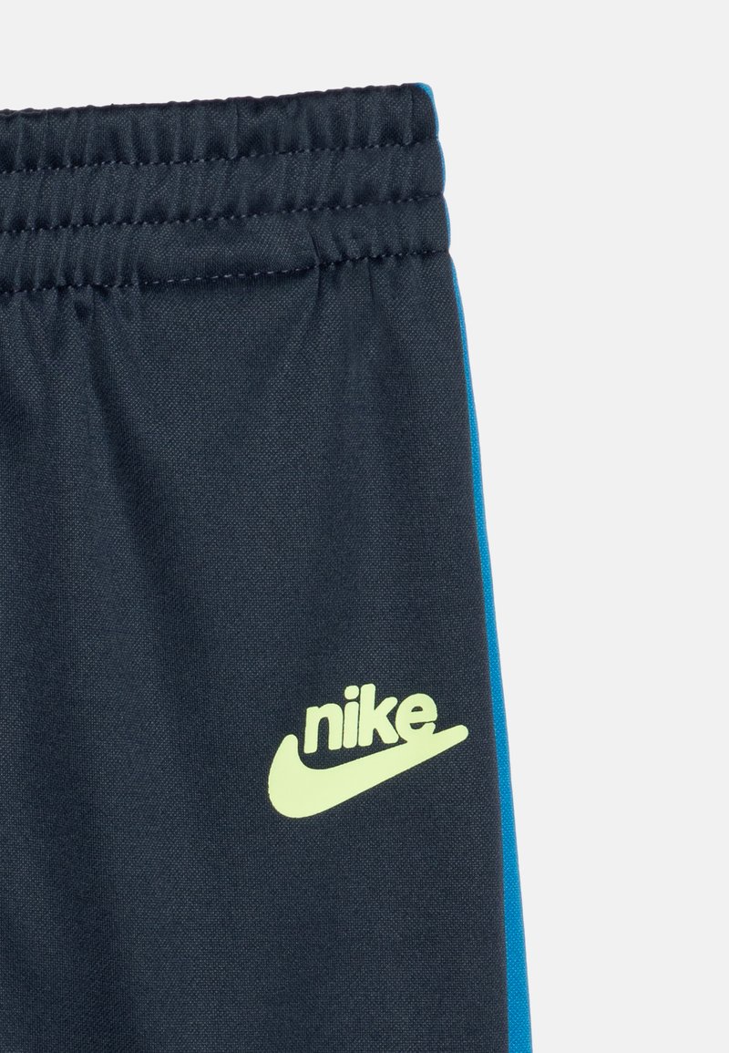 Pantalones cortos de deporte en color azul marino con un acabado texturizado, cinturilla elástica y un logotipo de Nike en verde lima en la parte delantera. Presenta franjas laterales en azul.