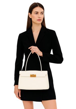 Sac à main en cuir blanc avec une forme structurée, une poignée supérieure et un fermoir en métal doré. L'arrière-plan est une tenue noire simple.