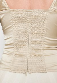 Beiges Satin-Kleid mit gerafften elastischen Details am Rücken, ausgestattet mit einem verdeckten Reißverschluss und einer glatten Textur.