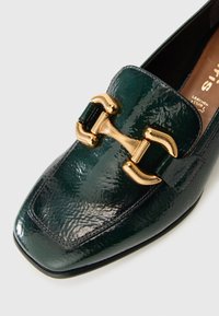 Mocassino in pelle lucida verde scuro con punta quadrata e dettagli in oro a forma di morso, che mostrano cuciture e parte della soletta.