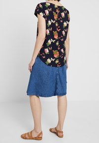 Navy kukkapaidan lyhyet hihat, yhdistettyinä farkkuhameeseen. Paita esittelee vaaleanpunaisia ja vihreitä kukkia, ja hameella on levenevä muoto.