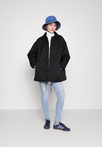 Sort, oversized jakke med lommer og snore, parret med lyseblå ripped jeans og blå bøttehat. Mørke sneakers fuldender looket.
