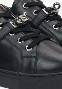 Černé kožené tenisky se stříbrným kováním, plochými černými tkaničkami a oky. Mají texturovaný materiál a gumovou podrážku.