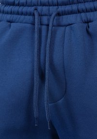 Pantaloni della tuta blu navy realizzati in un tessuto morbido e testurizzato, con vita elastica e cordini regolabili, e dettagli con tasche laterali.